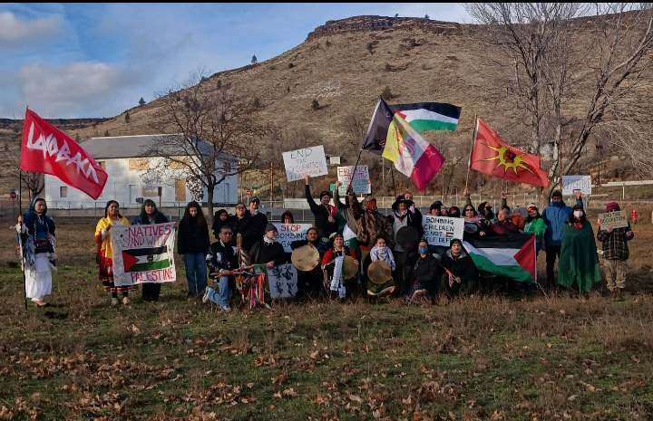 About 30 people huddle for a photo holding signs and Palestinian flags.