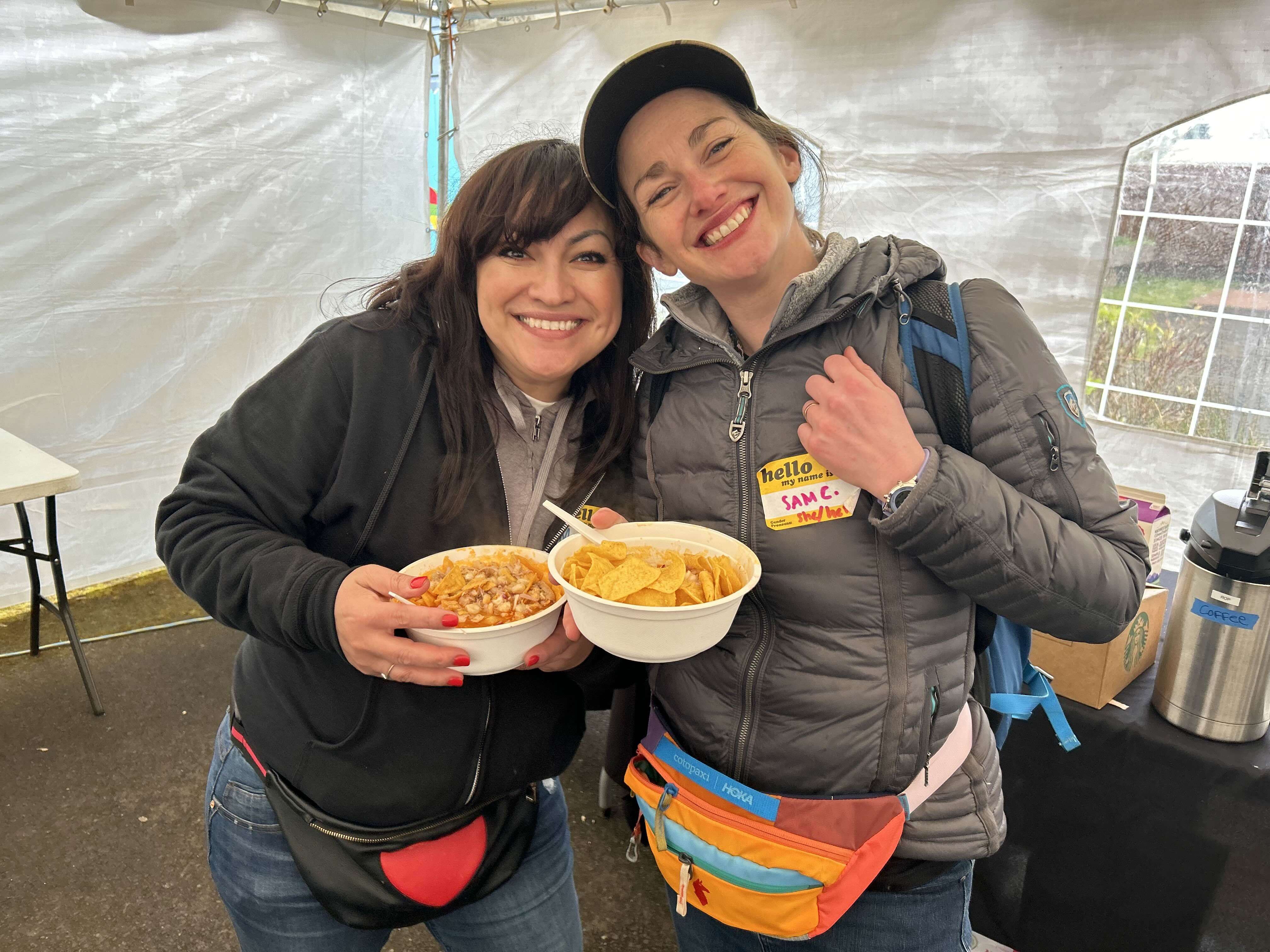 Two people smile for the camera holding up bowls of pozole.