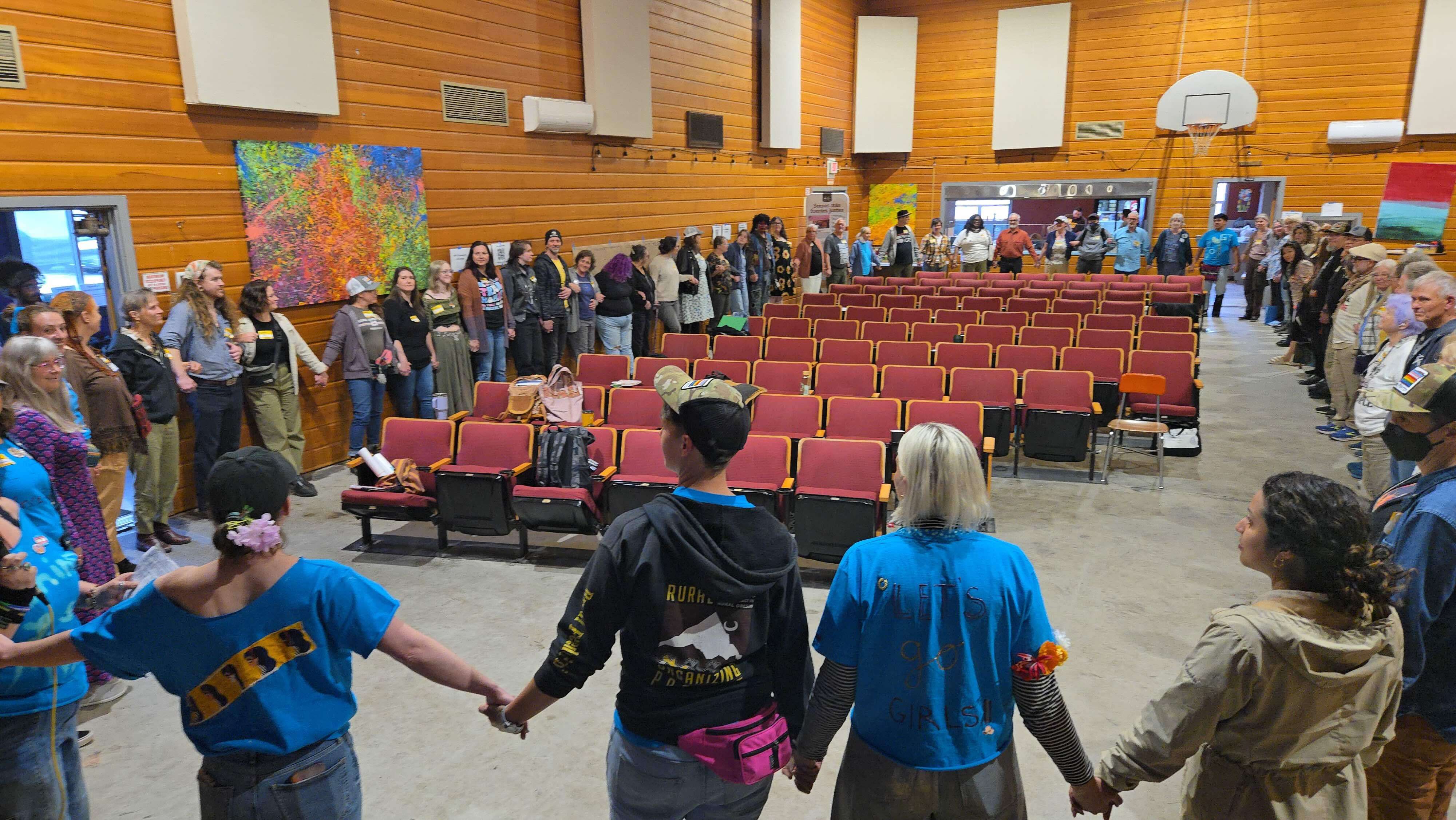 The Caucus stands in a large circle, all holding hands.